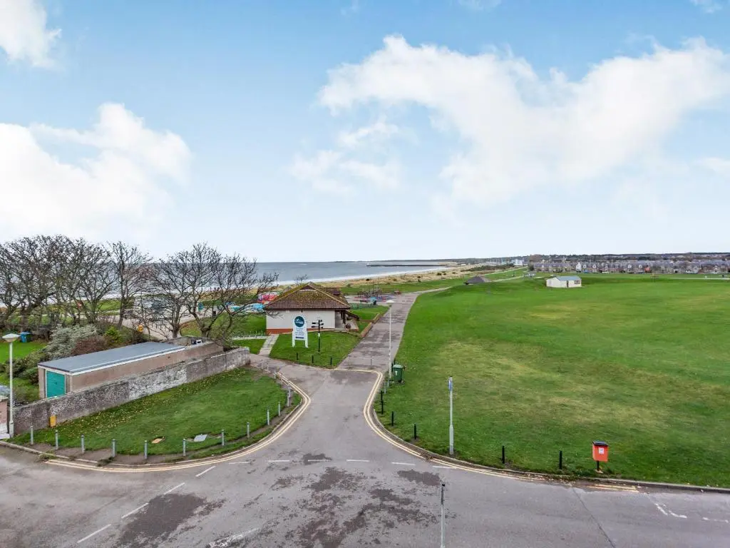 an empty road in front of a field and the ocean at Moray Firth View in Nairn