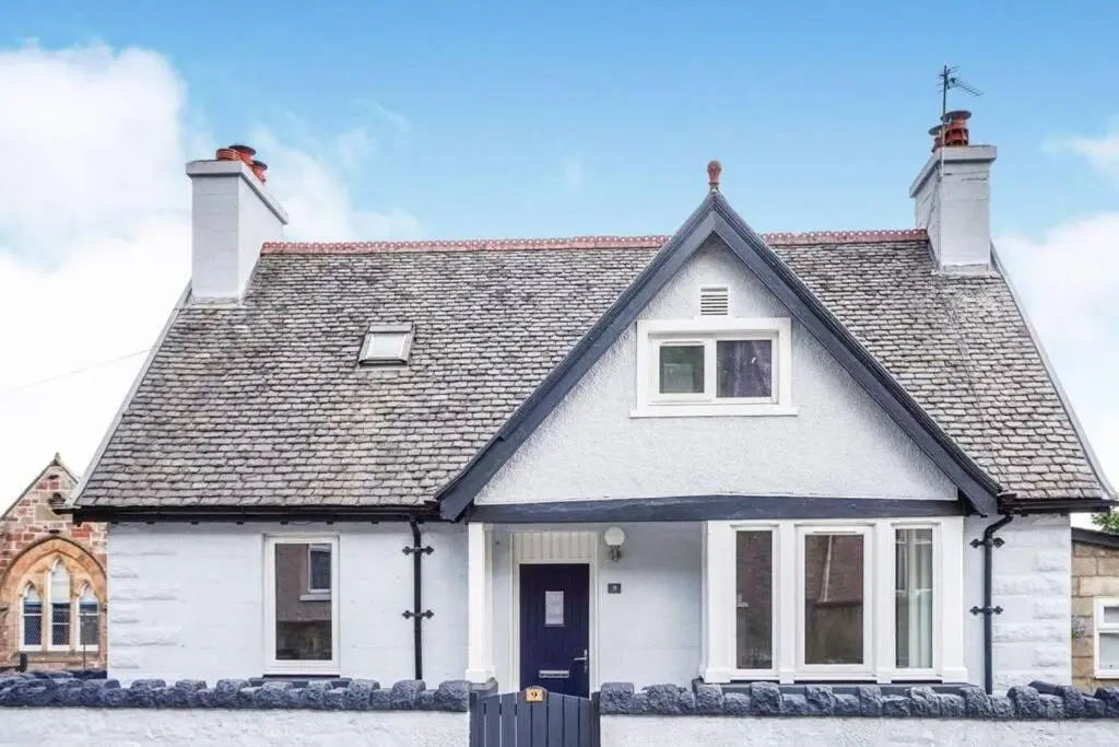 a white house with a black roof at Seacot Cottage in the heart of the Highlands in South Kessock