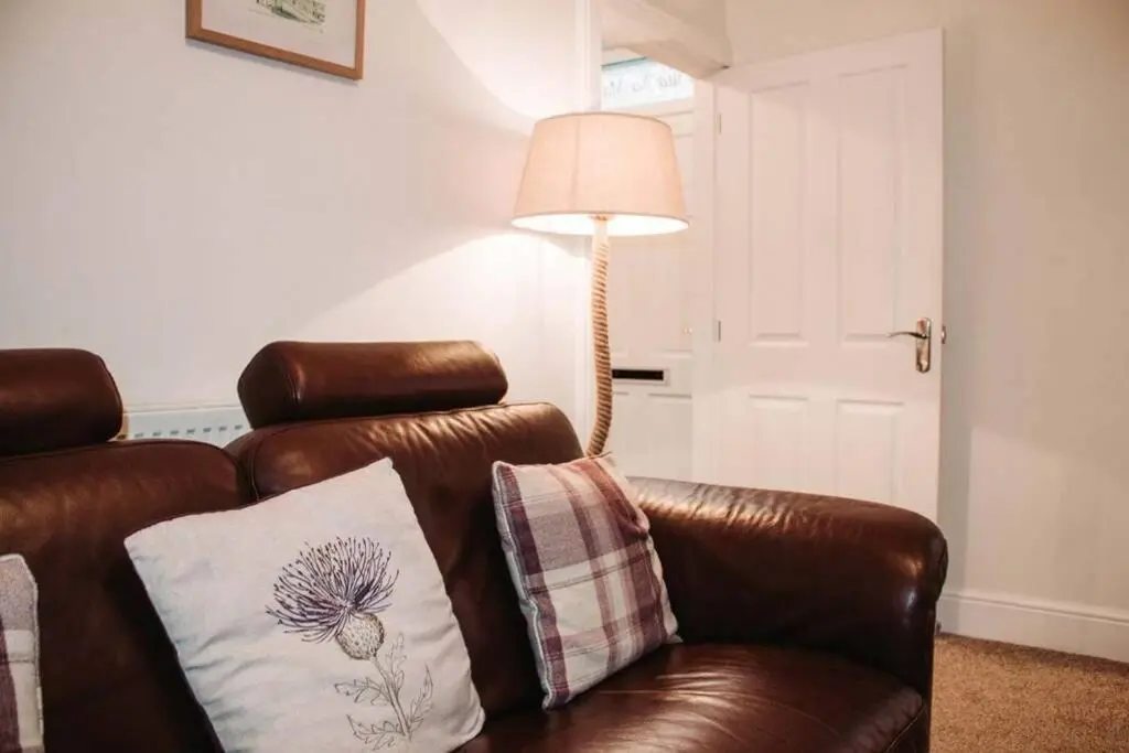 a brown leather couch with a pillow and a lamp at Craigewan Cottage Seatown Cullen in Cullen