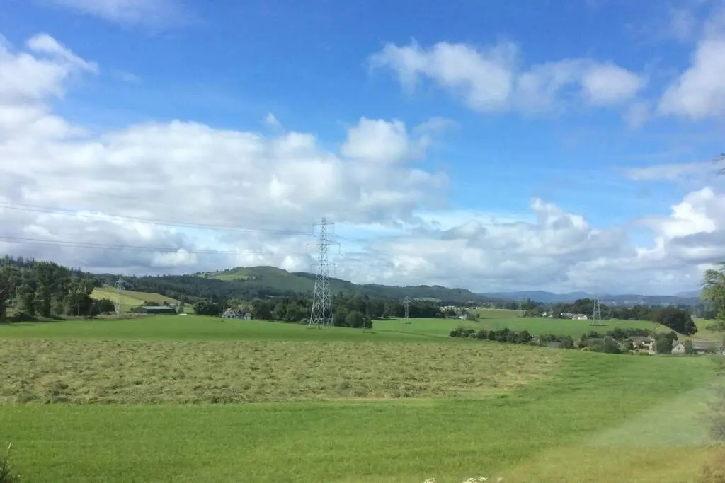 a green field with a electricity transmission tower in the distance at The Nest - Near Inverness & Loch Ness in Inverness