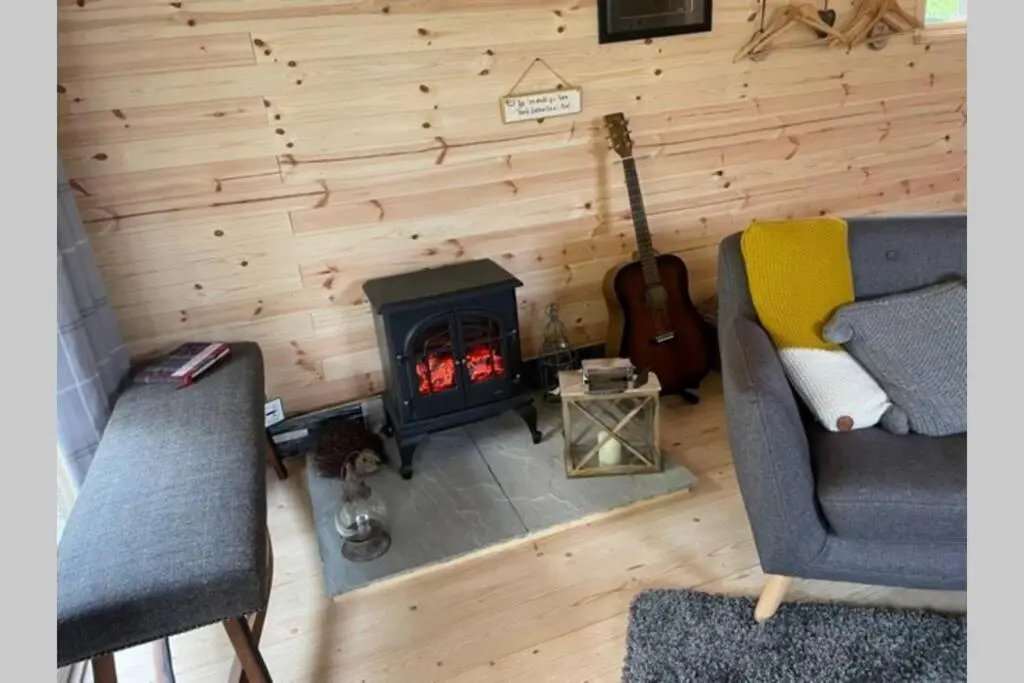 a living room with a fireplace and a couch and a guitar at Coorie Doon Cabin! Great Scottish Welcome in Fort Augustus