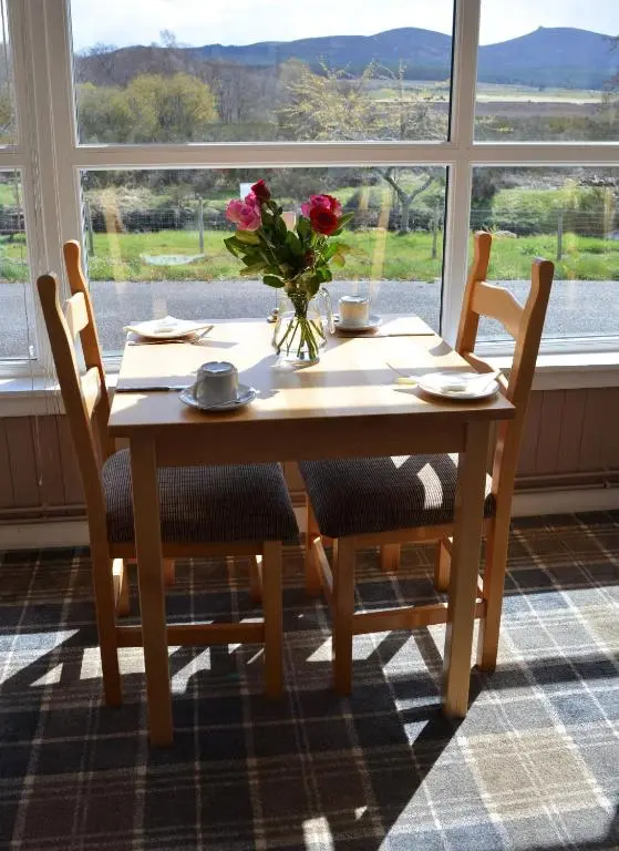 a wooden table with chairs and a vase with flowers at Feughside in Strachan