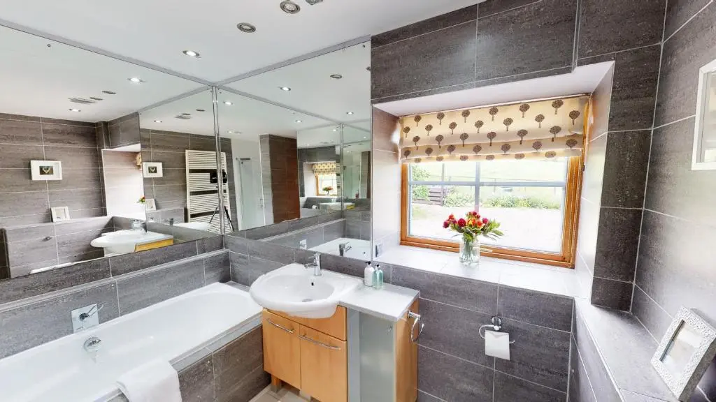 a bathroom with a tub and a sink and a mirror at The Eagle's Nest - large house with hot tub and sauna in Boat of Garten