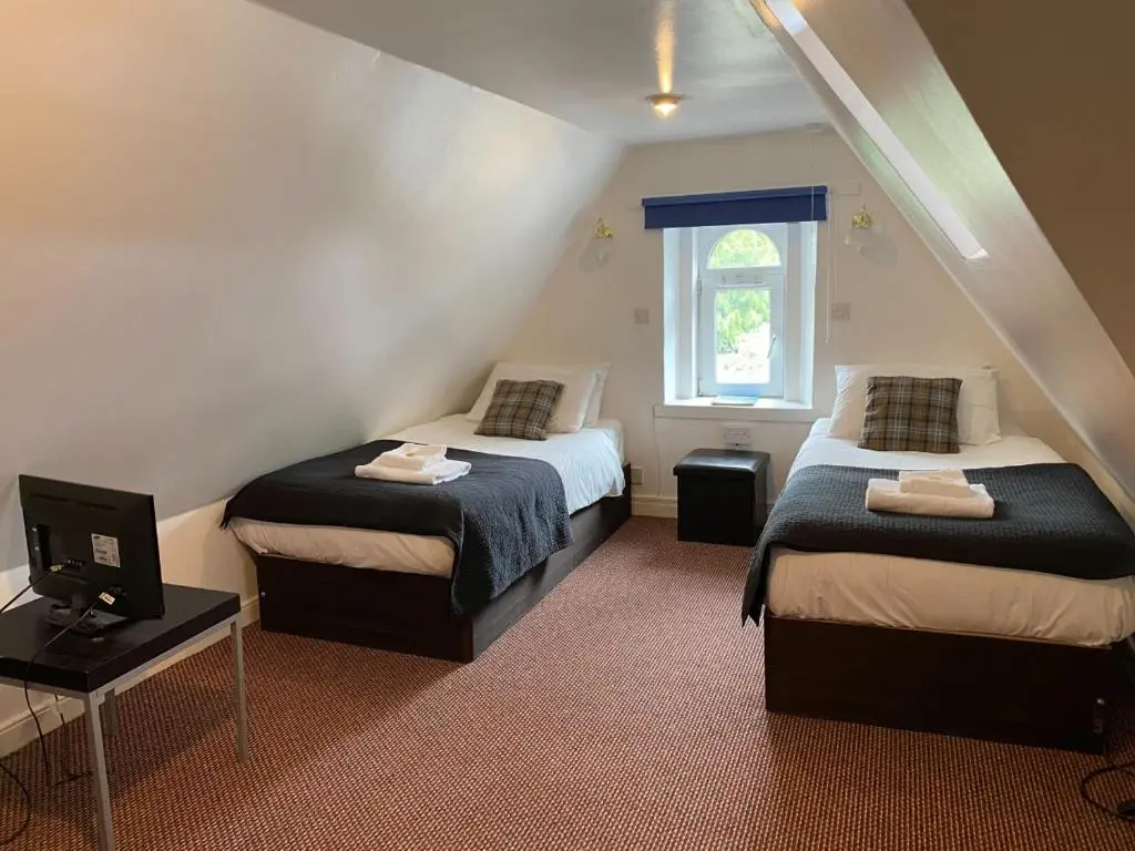 a bedroom with two beds and a tv and a window at Richmond House Hotel in Fort Augustus