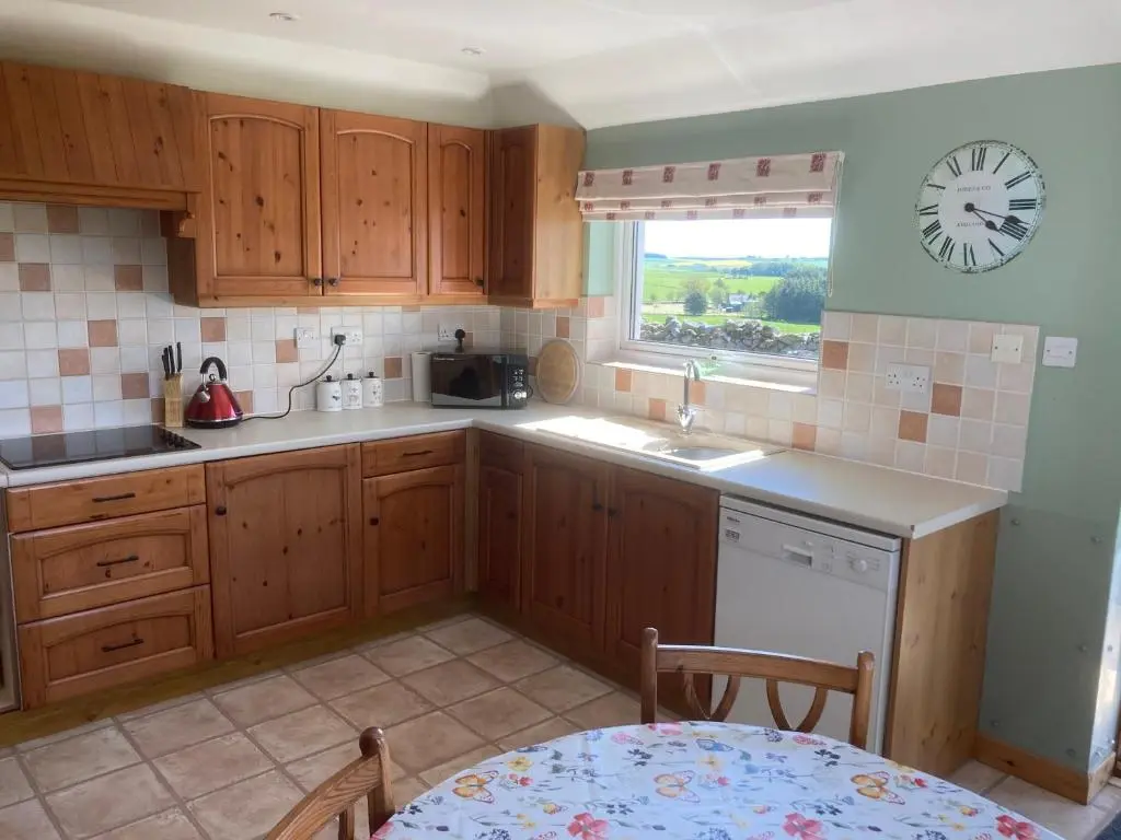 a kitchen with wooden cabinets and a clock on the wall at Meikle Aucheoch Holiday Cottage, plus Hot Tub, Near Maud, in the heart of Aberdeenshire in Peterhead