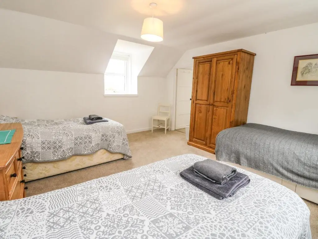 a bedroom with two beds and a wooden cabinet at Storkery Cottage in Aberdeen