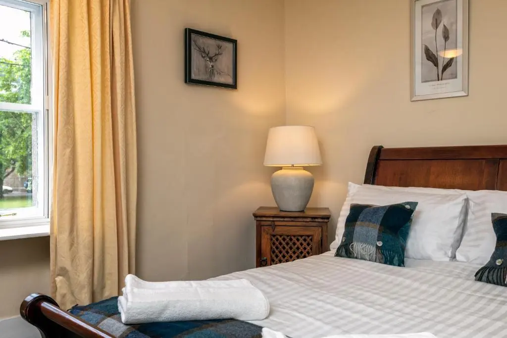 a bedroom with a bed and a lamp and a window at The Green Inn Rooms in Ballater