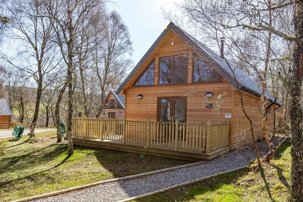 a log cabin in the woods with a porch at Thistle Lodge 21 with Hot Tub in Belladrum