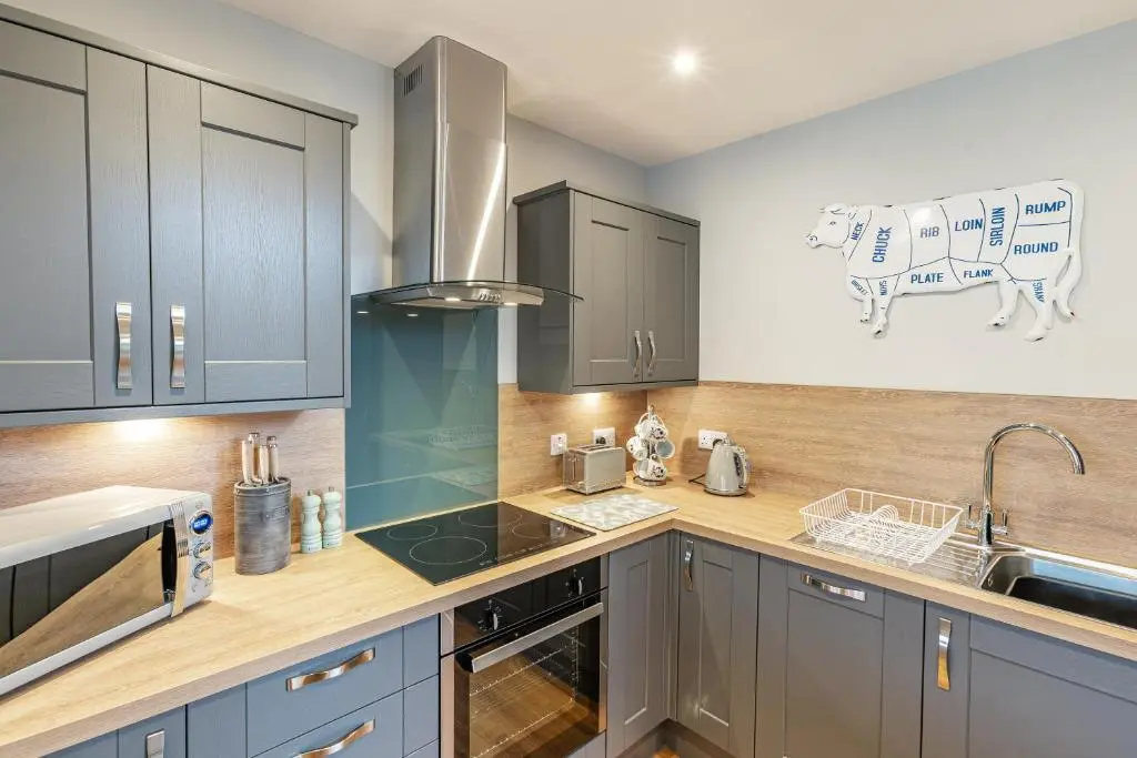 a kitchen with gray cabinets and a cow on the wall at Thistle Lodge 21 with Hot Tub in Belladrum