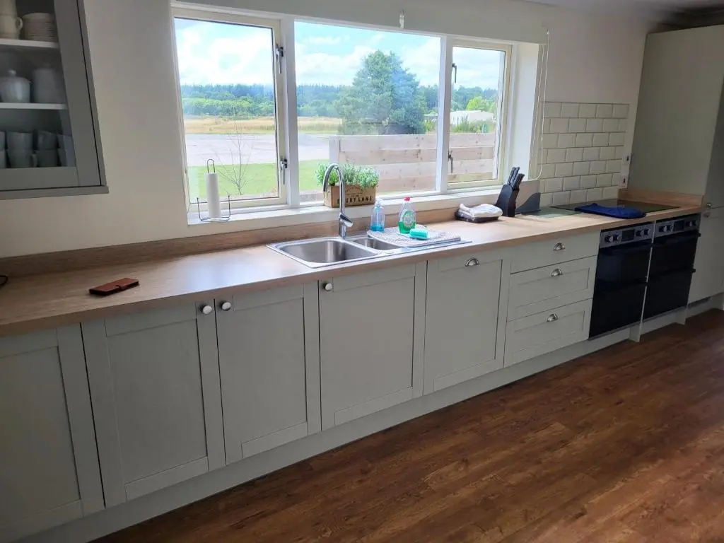 a kitchen with white cabinets and a sink and two windows at The Farmhouse, 6 bed property, Forres in Forres