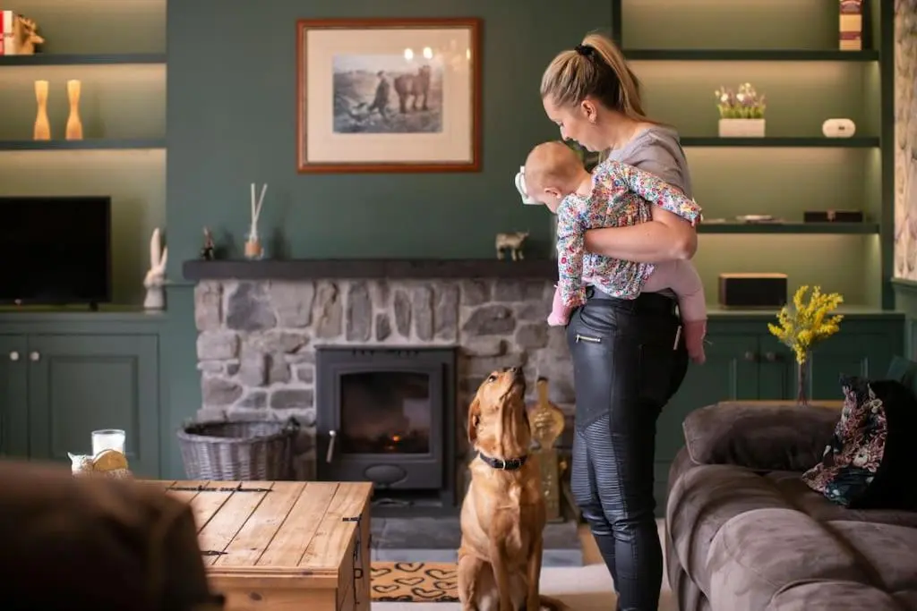 a woman holding a baby in a living room with a dog at Calm Scottish Country Escape with Hot Tub Sleeps 6 in Inverness
