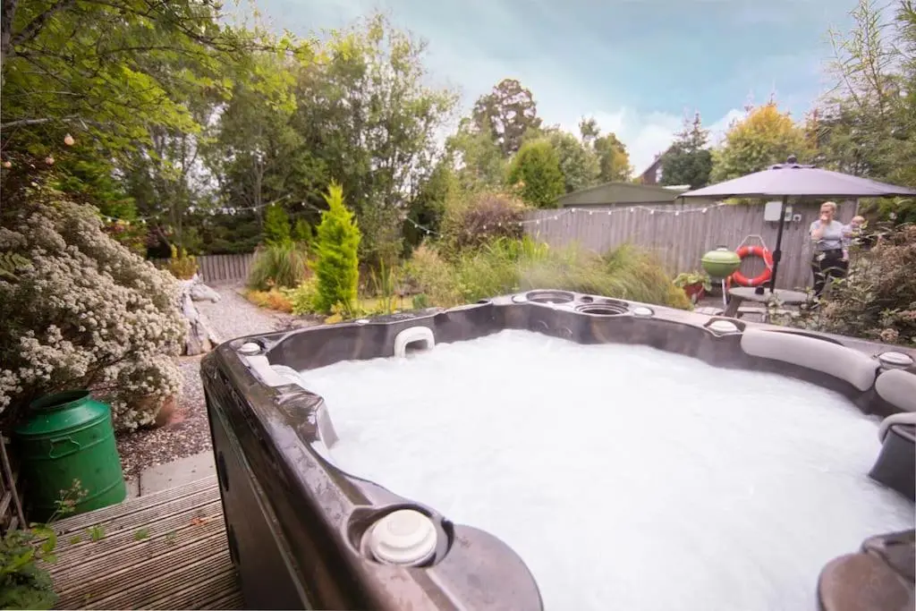 a hot tub in a garden with a person standing next to it at Calm Scottish Country Escape with Hot Tub Sleeps 6 in Inverness