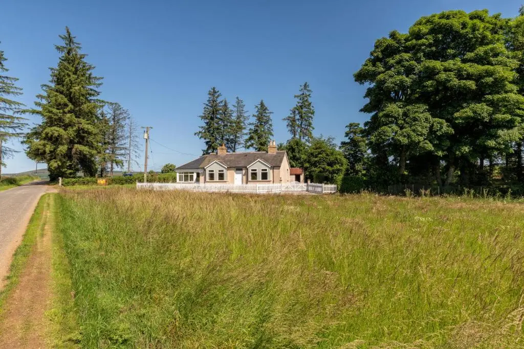 a house in a field next to a road at Stunning, Remodelled Cottage, Picturesque Location in Duncanston