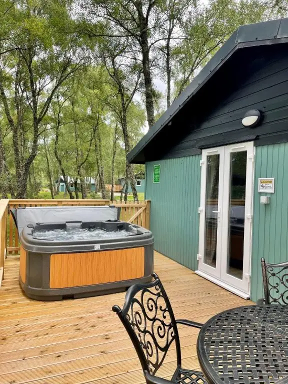 a hot tub on a deck with a table and chairs at Fern Lodge 2 with Hot Tub in Belladrum