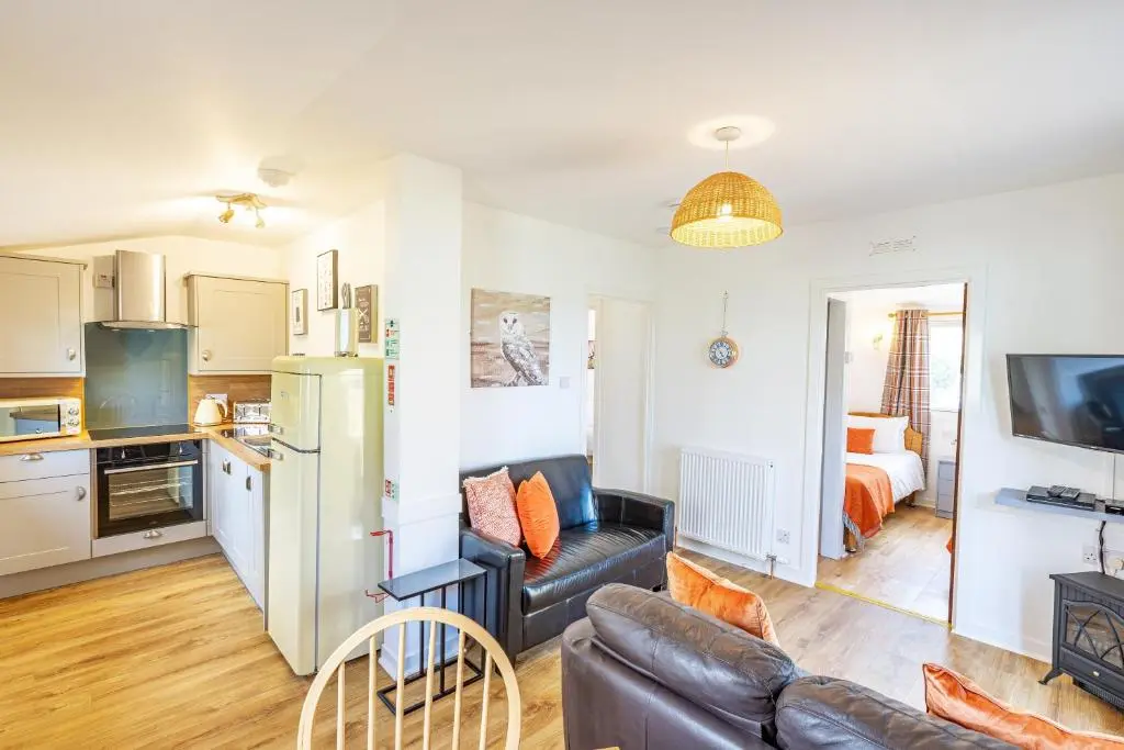 a living room with a couch and a kitchen at Fern Lodge 2 with Hot Tub in Belladrum