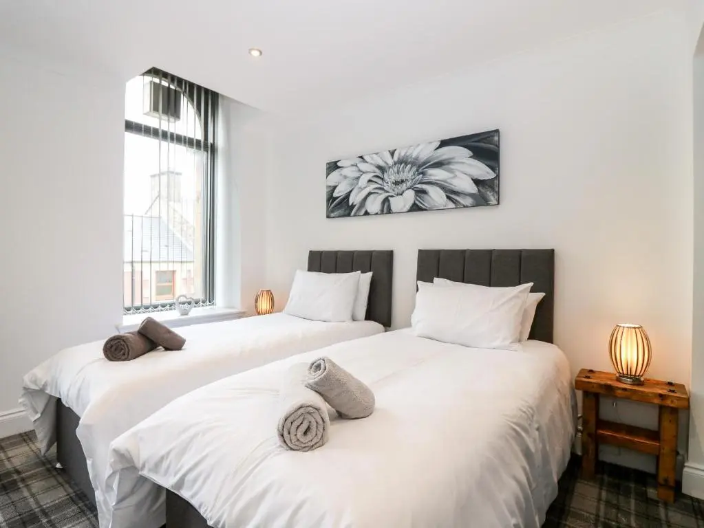two beds in a room with white walls and a window at The Clock Tower at The Institute Executive Apartments in Keith