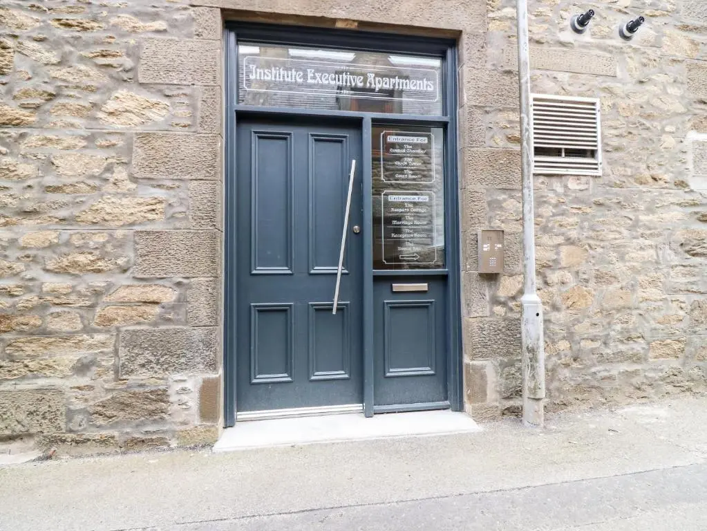 a blue door on a stone building with a sign above it at The Keepers Cottage at The Institute Executive Apartments in Keith