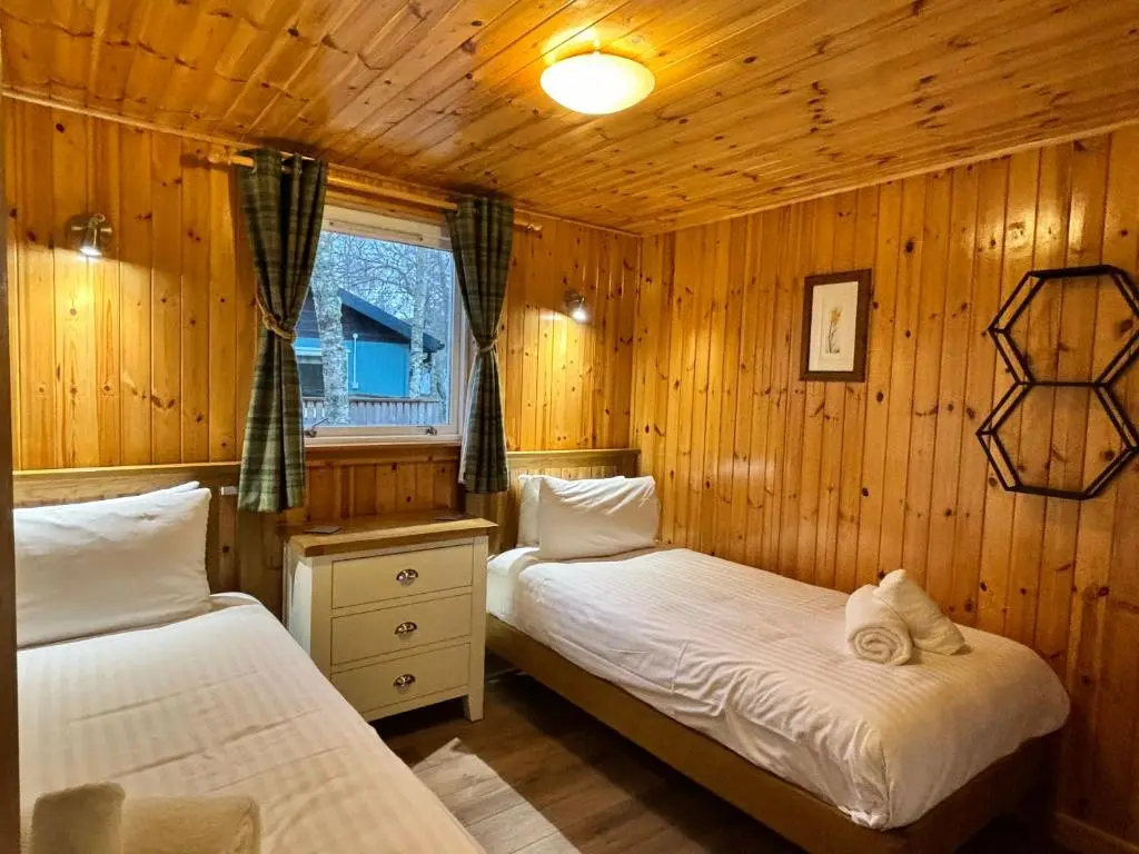 two beds in a room with wooden walls at Bracken Lodge 6 with Hot Tub in Belladrum