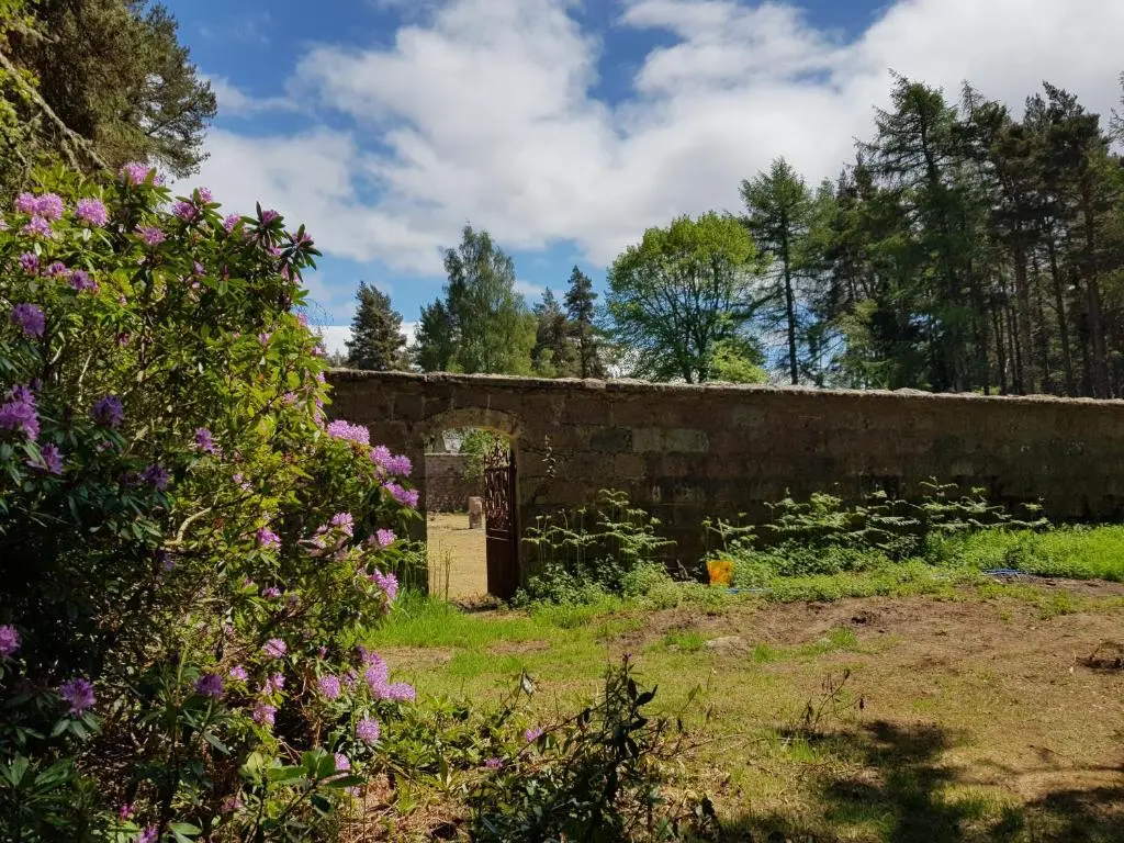 a garden with a brick wall and flowers at Cambus O' May Traditional Highland Hotel in Ballater