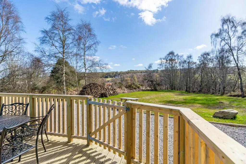 a wooden deck with a table and chairs and a field at Heather Lodge 17 with Hot Tub in Belladrum