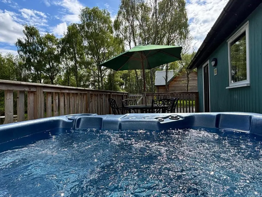 a pool with a green umbrella and a table with a chair at Heather Lodge 17 with Hot Tub in Belladrum