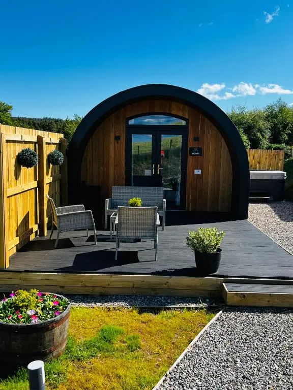 a wooden deck with two chairs and a building at Highland Premier Glamping Pods in Beauly