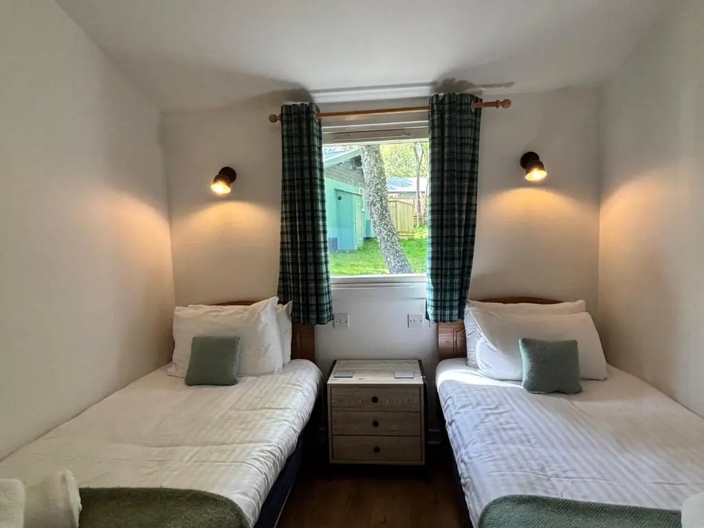 two twin beds in a room with a window at Fern Lodge 11 with Hot Tub in Belladrum
