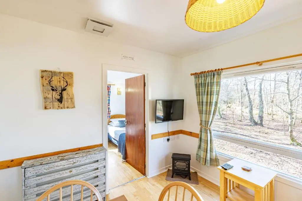 a living room with a table and a window at Fern Lodge 11 with Hot Tub in Belladrum