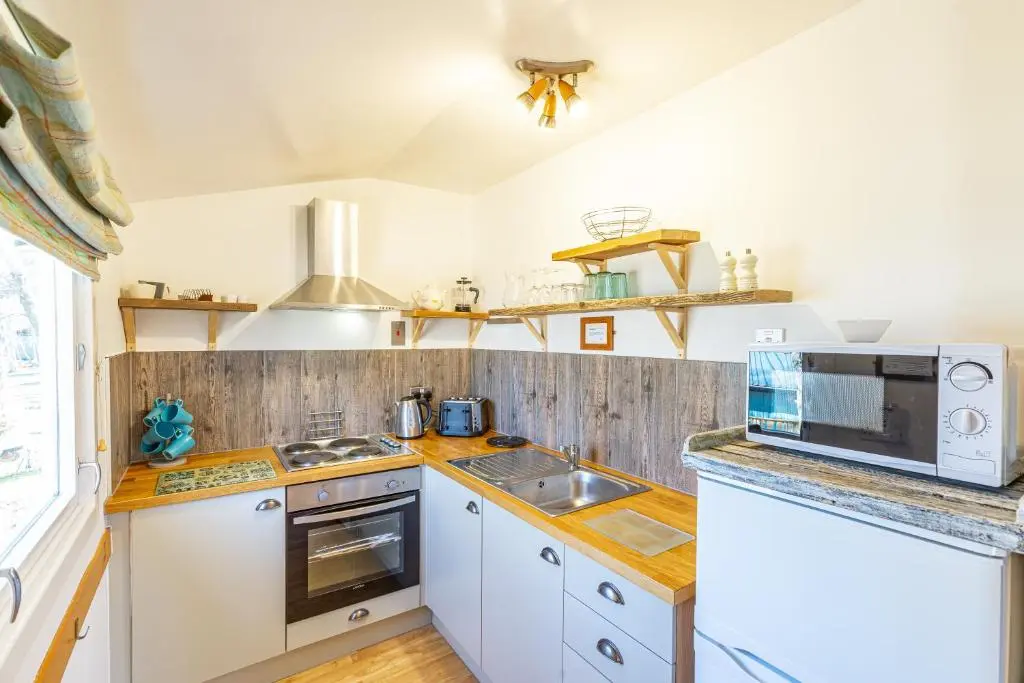 a kitchen with white cabinets and a microwave at Fern Lodge 11 with Hot Tub in Belladrum
