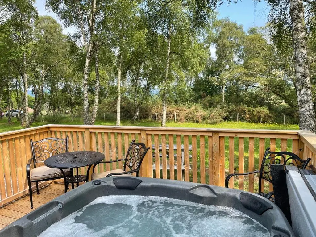 a hot tub on a deck with a table and chairs at Bracken Lodge 16 with Hot Tub in Belladrum