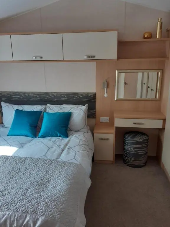 a bedroom with a bed with blue pillows and a mirror at RICK'S RETREAT static caravan near the beach with free wifi in Lossiemouth