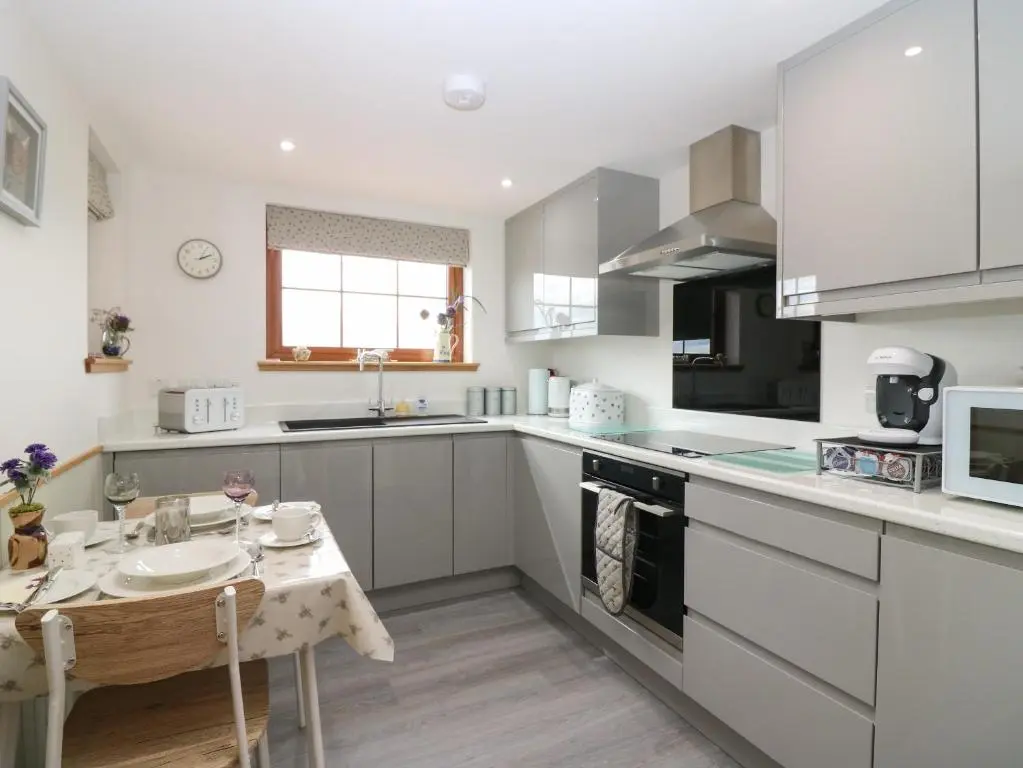 a kitchen with white cabinets and a small table at Garden Studio in Insch