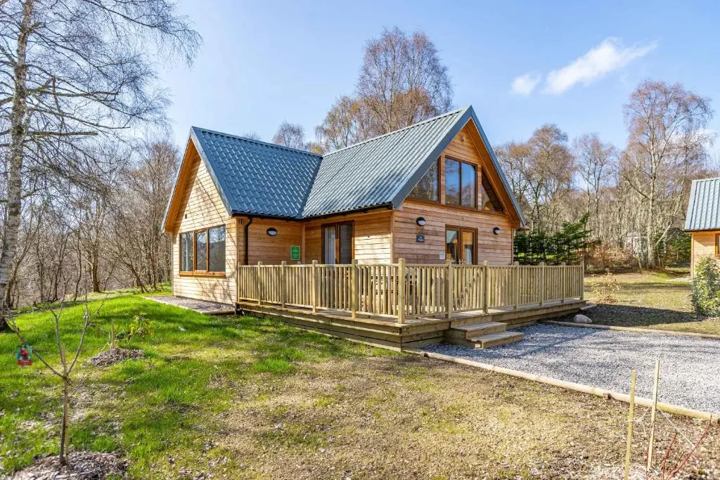 a log cabin with a porch and a house at Thistle Lodge 20 with Hot Tub in Belladrum