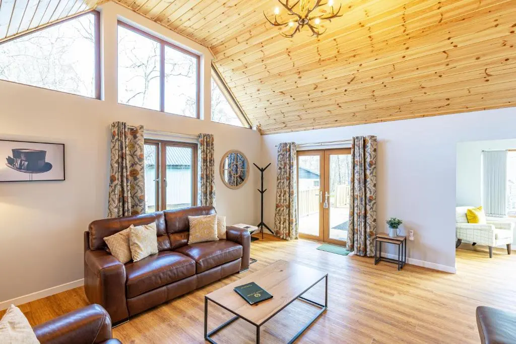 a living room with a leather couch and windows at Thistle Lodge 22 with Hot Tub in Belladrum