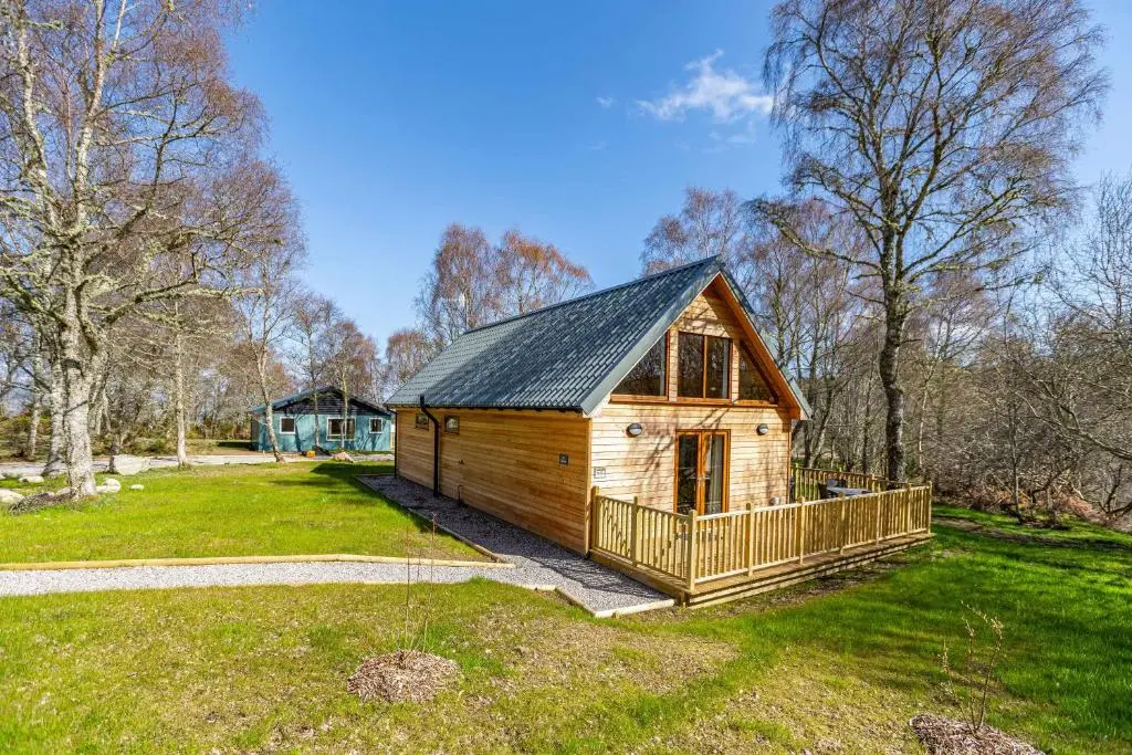 a small wooden cabin in a field of grass at Thistle Lodge 18 with Hot Tub in Belladrum