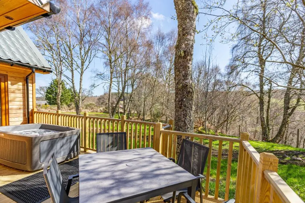 a patio with a table and chairs on a wooden deck at Thistle Lodge 18 with Hot Tub in Belladrum