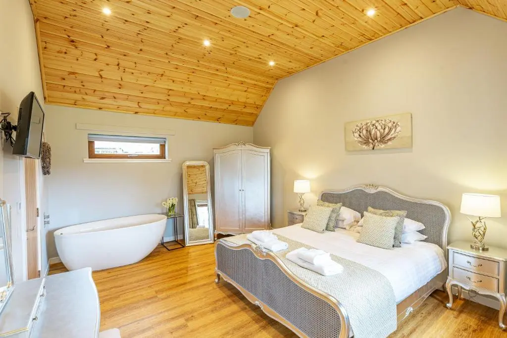 a bedroom with a large bed and a bath tub at Thistle Lodge 18 with Hot Tub in Belladrum