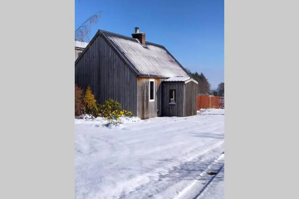 an old barn in the snow next to a street at Small cosy bothy in Dingwall