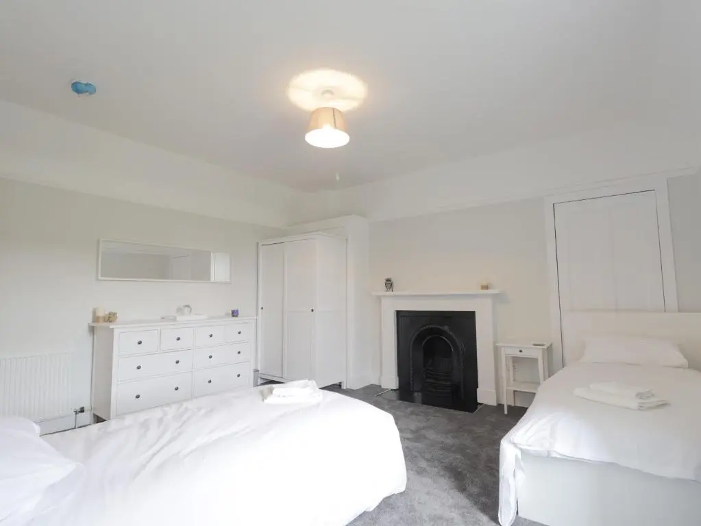 a white bedroom with two beds and a fireplace at Garden House - Brodie Castle in Forres