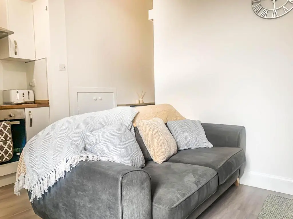a grey couch in a living room with a clock at The Rosebery Retreat By The Castle 1-Bed Apartment in Inverness