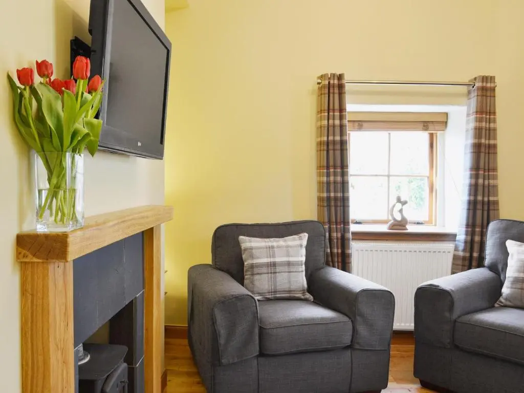 a living room with two chairs and a television at North Lodge Gate House in Urray