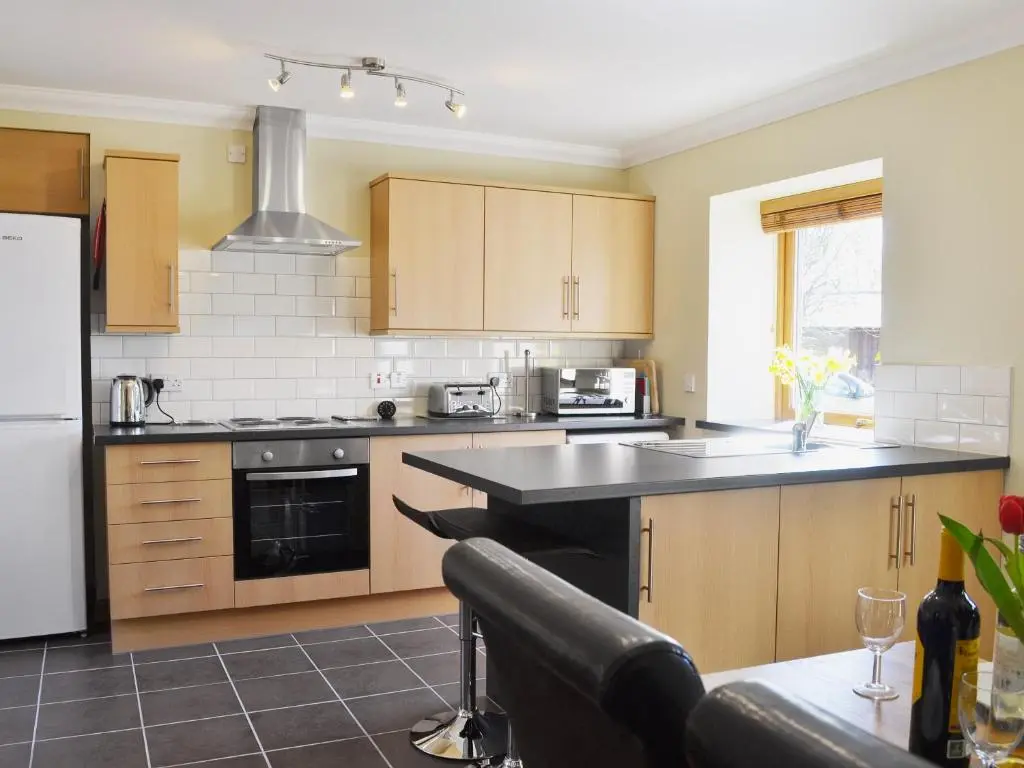 a kitchen with wooden cabinets and a black counter top at North Lodge Gate House in Urray