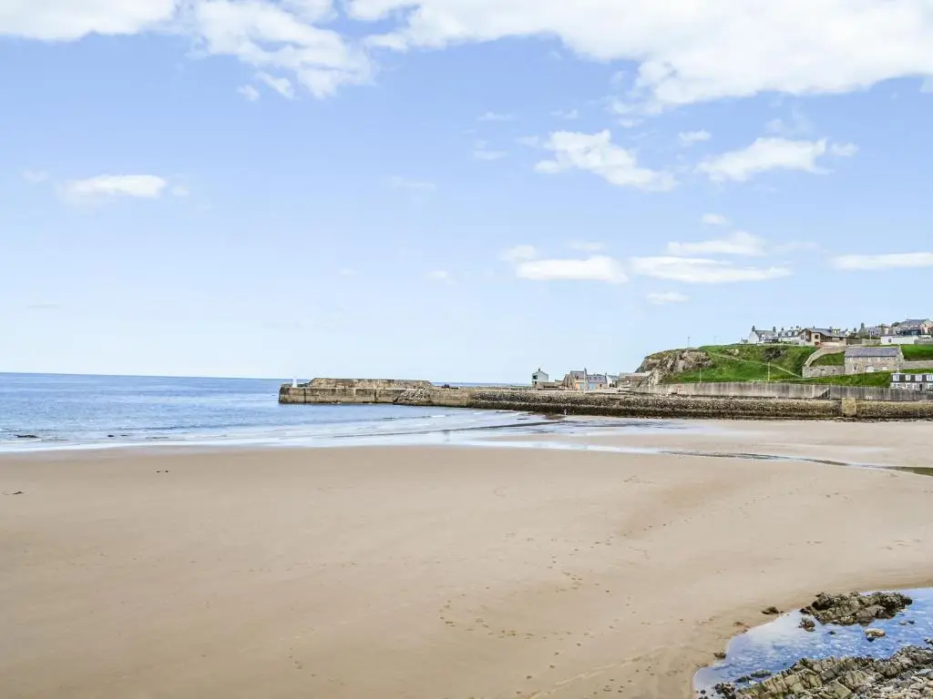 a sandy beach with a pier in the ocean at Needle Cottage in Cullen