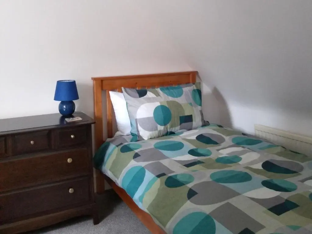 a bedroom with a bed with a blue lamp on a dresser at Needle Cottage in Cullen