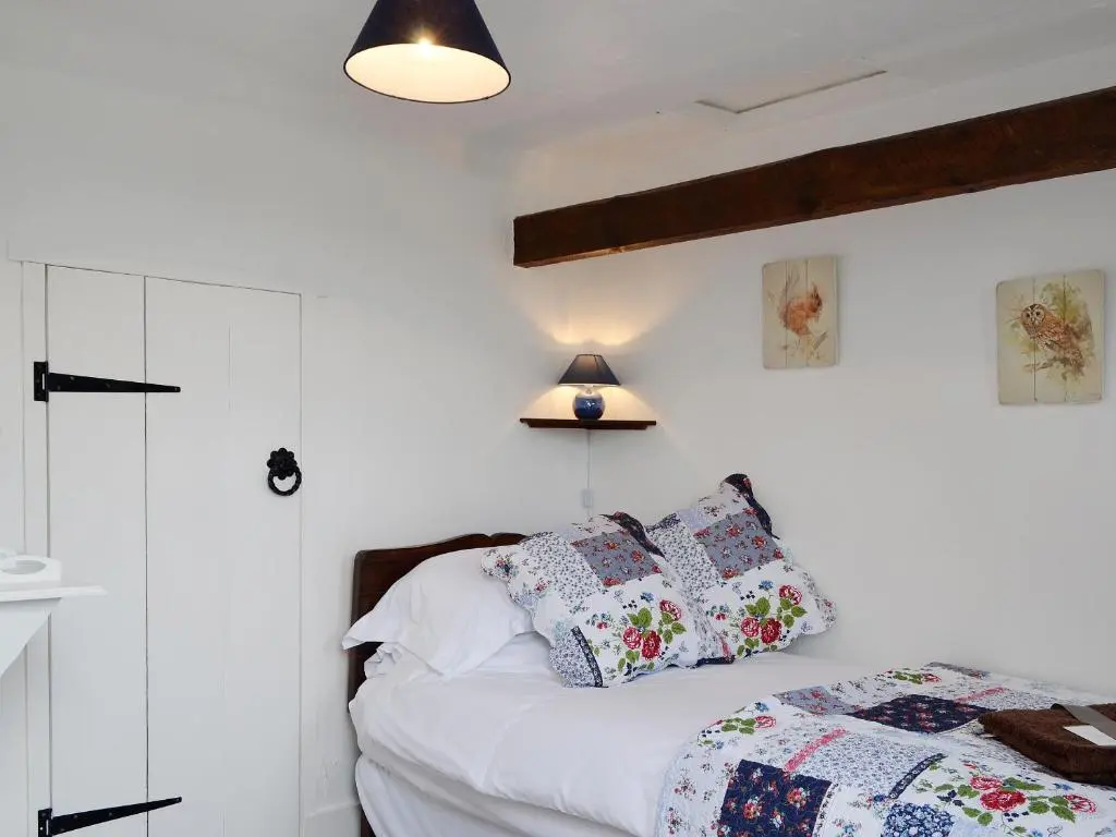 a bedroom with white walls and a bed with pillows at Woodside Cottage in Auchnastank