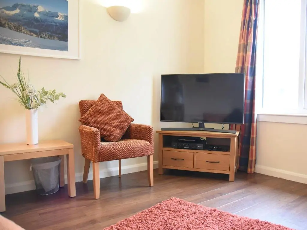 a living room with a television and a chair at Bonnie Doon in Aviemore