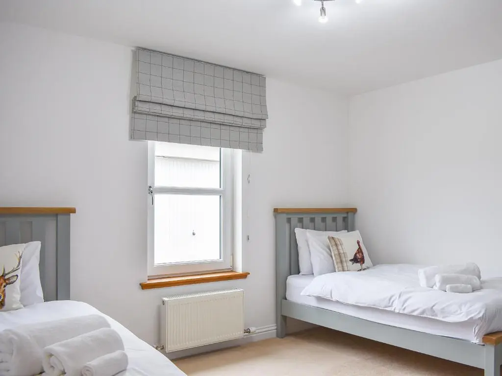 a bedroom with two beds and a window at 1 Dalbuaick Farm Cottage in Carrbridge