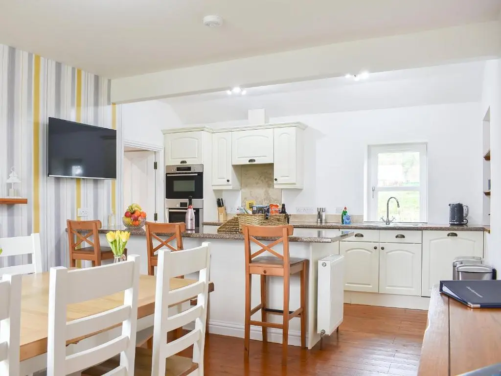 a kitchen with white cabinets and a table and chairs at 1 Dalbuaick Farm Cottage in Carrbridge
