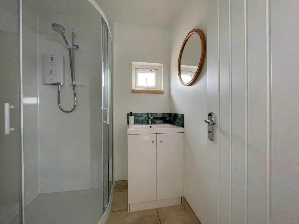 a bathroom with a shower and a sink and a mirror at Sunrise Summerhouse in Hilton of Cadboll