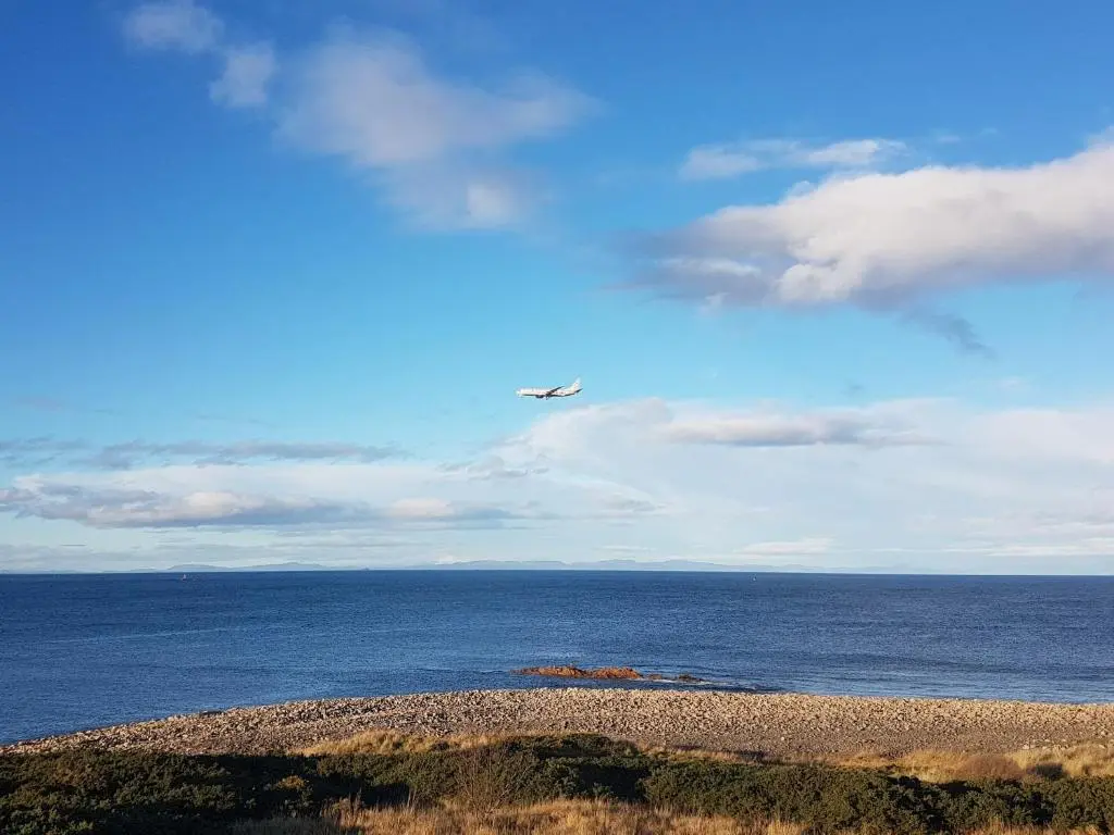 an airplane flying over the ocean with a beach at Aurora in Lossiemouth